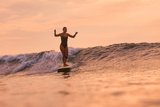 Woman Gliding On Wave At Golden Hour, Capturing Cinematic Sunset Vibe With Poised Stance And Warm Reflections