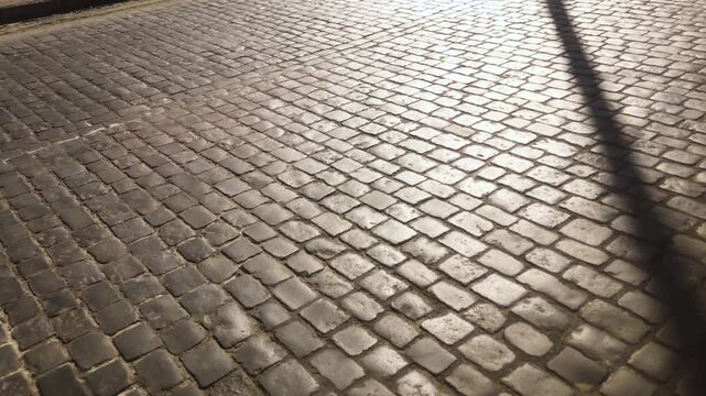 Old cobblestone pavement surface with sunlight and diagonal shadow in slow motion.