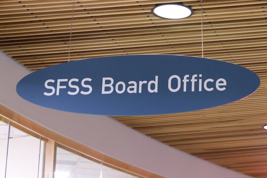 SFSS Board Office oval hanging sign suspended by chains from a wood slat ceiling at the SFU downtown Vancouver campus