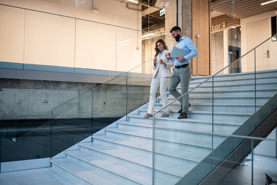 Business colleagues walking down office stairs talking and smiling