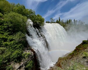 Fototapeta premium Breathtaking view of a powerful majestic waterfall cascading down rocky cliffs with a beautiful rainbow in the mist.