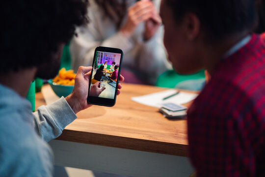 Person holding a smartphone, viewing friends interacting and having fun on the screen, capturing social moments at a gathering