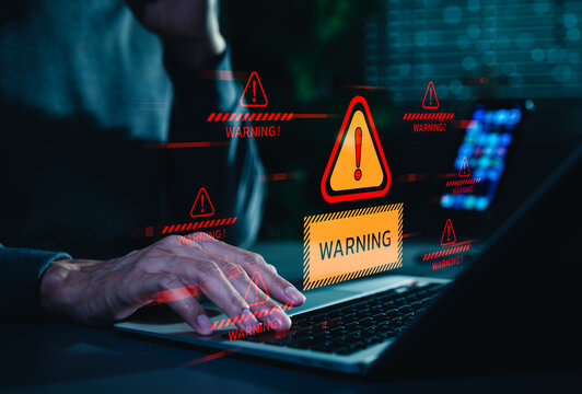 Cybersecurity warning alert concept. A person using laptop as digital threat notifications appear, representing malware attack, data breach risk, and system security vulnerability in online networks.