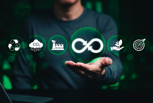 Circular economy concept. Businessman holding glowing infinity symbol with icons for carbon reduction, recycling, green factory, and renewable energy for sustainable corporate goals. sustainability,
