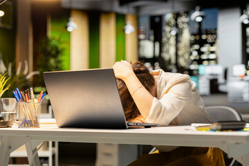 Businesswoman struggling to stay awake after an intense workload, lounges across desk at midnight....