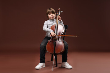 Cute little boy playing violoncello on brown background © New Africa