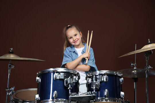 Little girl with drumsticks and drum kit on brown background