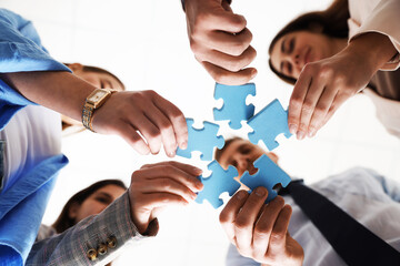 Obraz premium Team building. Group of businesspeople putting puzzle pieces together against blurred white background, bottom view