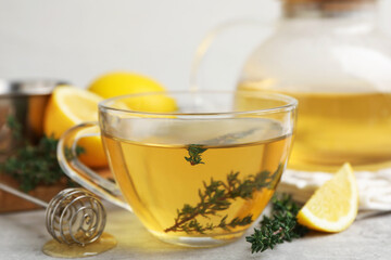 Obraz premium Fresh thyme tea in glass cup, dipper and slice of lemon on grey table, closeup