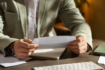 Man opening envelope with letter at wooden table indoors, closeup
