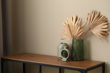 Fototapeta premium Beautiful vases and other decor on wooden table near beige wall indoors, space for text