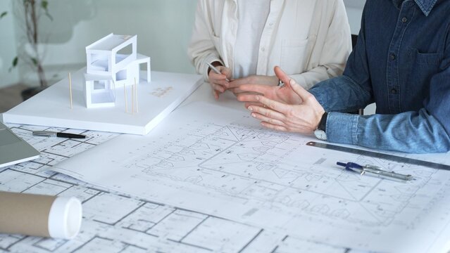 Architects discussing building plans, reviewing blueprints and architectural models, brainstorming design ideas for a new residential or commercial construction project