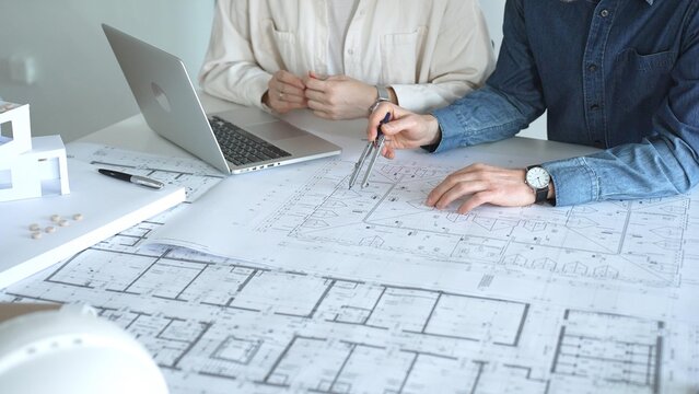 Architects engaging in a professional meeting, reviewing detailed blueprints on a table, utilizing a laptop, and collaborating on building design and construction planning