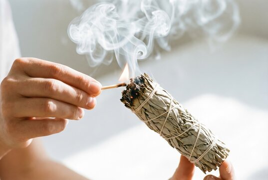 Hands using wooden match to light dried white sage smudge stick to cleanse energy