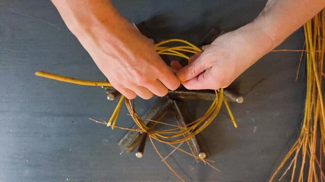 Top down view of hands weaving a rustic wreath base from natural willow branches, authentic DIY home craft hobby and decoration making.