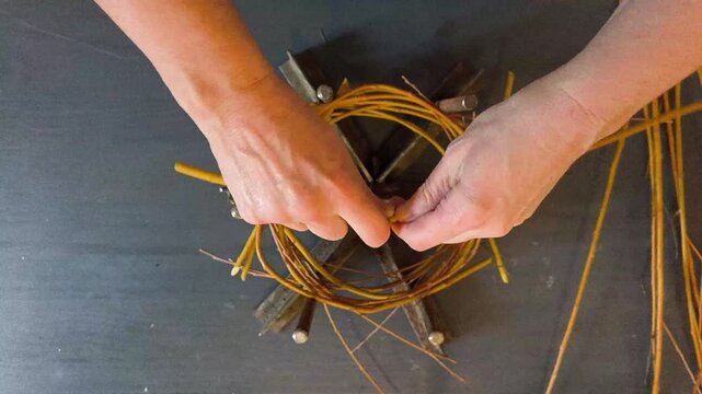 Top down view of hands weaving a rustic wreath base from natural willow branches, authentic DIY home craft hobby and decoration making.