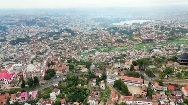 Aerial drone view above Antananarivo with the city skyline spread across surrounding hills, showing dense urban neighborhoods and the large historic palace complex overlooking Madagascar's capital