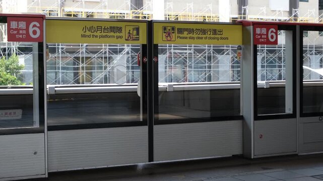 Taipei Metro platform screen doors in Taiwan with safety signage and arriving train behind glass barriers. Modern MRT station infrastructure with bilingual warnings and controlled boarding system.