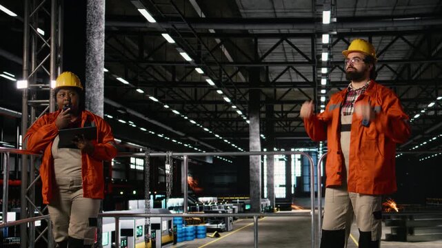 Portrait of personnel in helmet and safety glasses reviewing industrial design in a machinery hall. Massive steel beams and metalwork define heavy industry warehouse, engineering expertise.