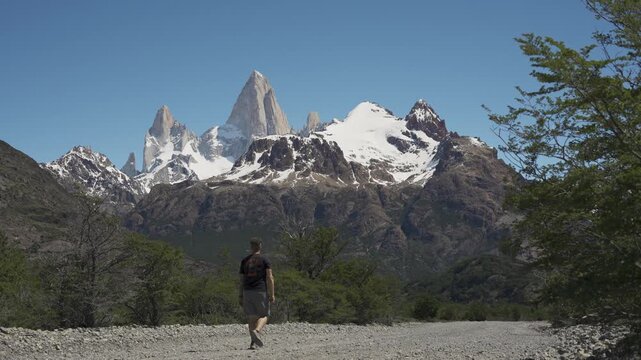 Man walking on a dirt road toward sharp snowy mountain peaks of Mount Fitz Rin nature. El Chalten, Patagonia, Argentina