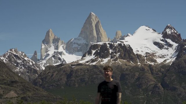 Close up of a man walking in front of sharp snowy mountain peaks of Mount Fitz Roy focus. Patagonia, Argentina