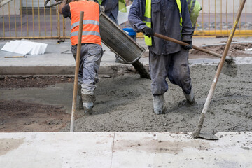 Construction workers pour wet cement onto a busy city street during daytime