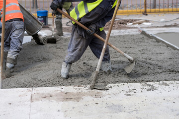 Construction workers pour wet cement onto a busy city street during daytime