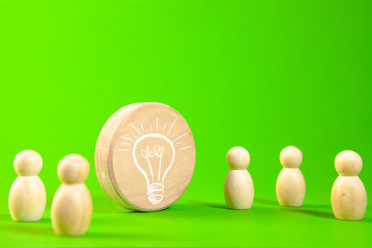 Wooden figures of people and light bulb on a green background. Business concept