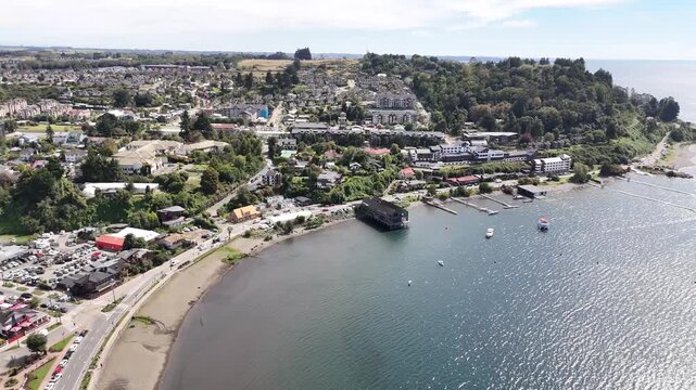 Cinematic aerial pan from left to right over the shoreline of Lake Llanquihue, revealing the vibrant downtown architecture, waterfront piers, and hotels of Puerto Varas, Chile