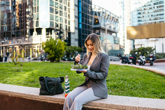 Businesswoman eating a fresh salad outdoors during her lunch break in the city