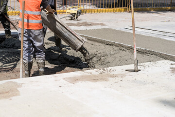 Construction workers pour wet cement onto a busy city street during daytime