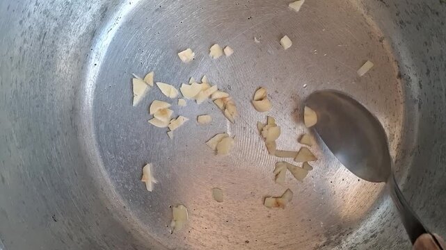 A person stirring chopped garlic in the bottom of a pan