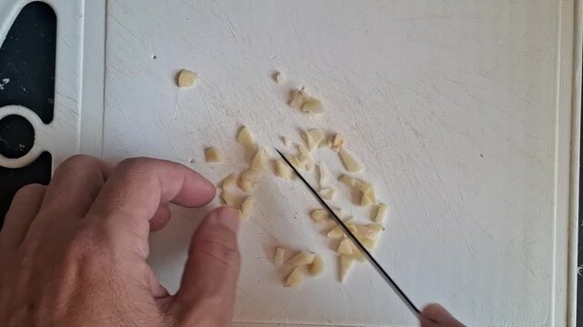 A person chopping garlic with a paring knife