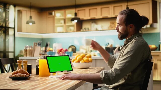 Mockup green screen on tablet screen in the kitchen at wooden table. Modern lifestyle with chroma key, infographic elements and digital tools, teleworking and multitasking indoors.