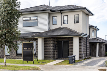 Fototapeta premium Modern suburban townhouse for sale in Melbourne, Australia with real estate signboard in front yard. Contemporary two storey home in a residential neighborhood representing the local housing market.