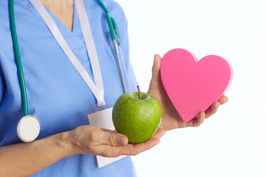 Close-up of a healthcare provider in scrubs holding an apple and a heart shape, focusing on the visual cues of medical expertise and nutritional guidance.