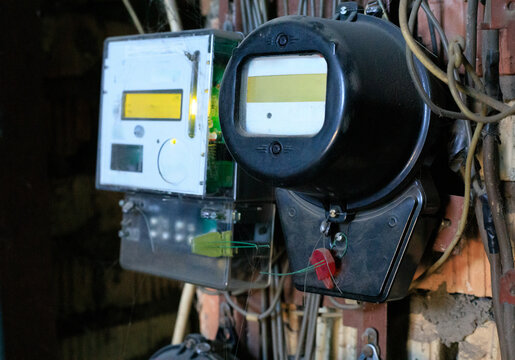 Old analog electricity meter stands alongside a modern digital replacement in a weathered interior