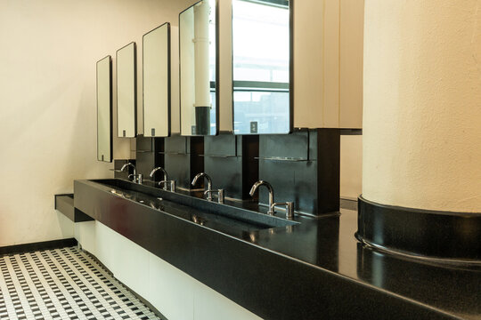 Modern public restroom interior with black granite sink counter, multiple faucets, mirrors, and clean geometric design. 