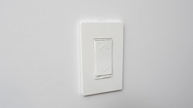 White light switch on a smooth wall, showing a gradual change in position across three frames, highlighting the action of turning lights on and off