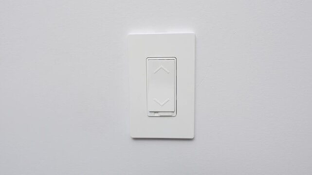 White light switch on a plain wall, showing upward and downward arrows indicating control for lighting adjustments in a modern interior setting