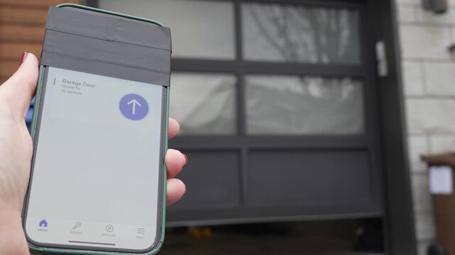 Hand holding smartphone displaying garage door control interface, showing gradual opening of garage door with interior tools and equipment visible