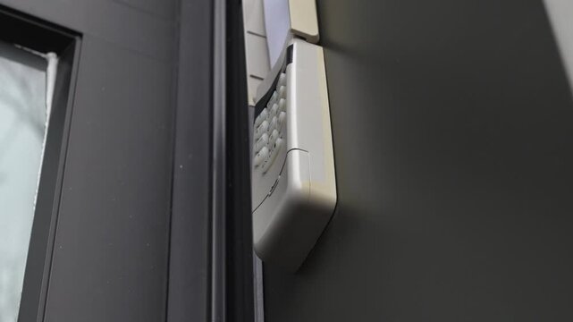 Security keypad mounted on a dark wall near a door, showcasing the entry system's buttons and design in a residential setting