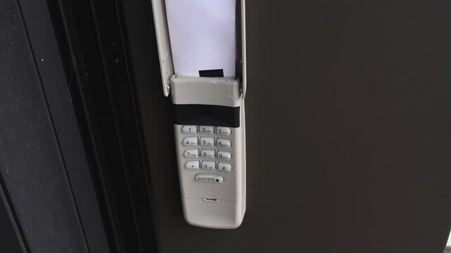 Security keypad mounted on a wall with a paper inside the compartment, showcasing the entry mechanism in a residential setting