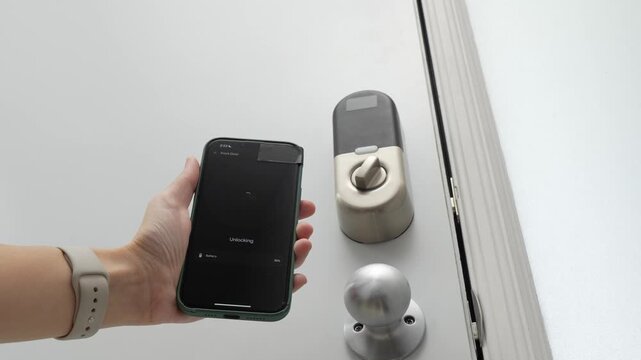 Hand holding smartphone near smart lock, displaying unlocking interface, showcasing modern technology in a contemporary indoor setting