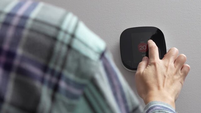 Individual adjusts smart thermostat settings, transitioning from 20 to 21 degrees Celsius, wearing a plaid shirt in a modern home interior