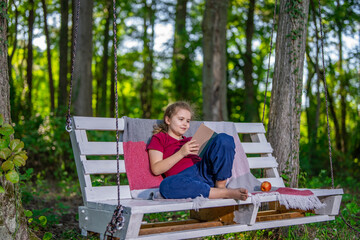 Fototapeta premium Child dreaming peacefully on swing in yard. Happy kid enjoying freedom and nature on swing. Girl resting on swing enjoying summer. Child sitting relaxed on playground swing.