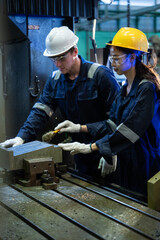 Diverse industrial engineers in hard hats and safety glasses operate a manual milling machine in a metalworking factory. Workers in jumpsuits use a brush to clean metal parts on a workbench © winnievinzence