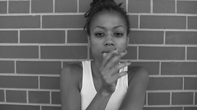 Defiant young woman smoking against a wall. Black and white. HD video.