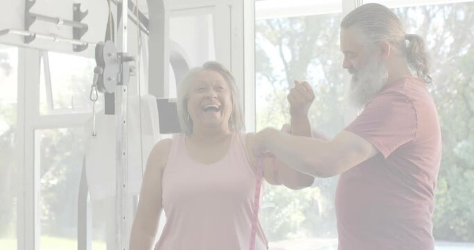 Mature man bringing red resistance band and wrapping woman's upper arm, enabling home rehab session