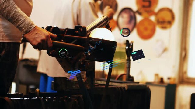 Glassblower rotating blowpipe reheating molten glass while helper handing tools shaping vessel